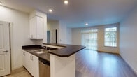 Located at 8509 Litt Dr SE in Lacey, Washington, this single-floor unit offers a clean, contemporary design with a thoughtful layout. The open-concept living and kitchen area forms the heart of the space, where light-toned hardwood-style flooring flows throughout, creating a cohesive and modern aesthetic.

The kitchen is well-appointed with stainless steel appliances, including a refrigerator, microwave, and range, all complemented by crisp white cabinetry that extends to the ceiling for generous storage. Dark countertops provide a striking contrast against the white cabinets, and a peninsula island with an integrated sink and dishwasher serves as both a functional workspace and a casual dining or gathering spot.

The living area is bright and open, benefiting from natural light that streams in through a large sliding glass door fitted with vertical blinds. The door leads to an outdoor area, extending the sense of space and offering a seamless connection to the outside.

The bathroom features the same hardwood-style flooring, a wide vanity with dark countertops and white cabinetry, and a clean, minimalist finish throughout. Recessed lighting in key areas adds a polished touch to the overall interior. The unit presents a move-in ready, modern living environment in a well-situated Lacey location.