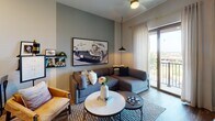 This single-floor residence showcases a thoughtfully designed interior with a cohesive modern aesthetic throughout. The living area serves as the social heart of the space, featuring warm wood-look flooring, a ceiling fan, and large sliding glass doors that open to a private balcony with outdoor views and abundant natural light. A sectional sofa, pendant lighting, and curated wall art contribute to the room's relaxed yet sophisticated character.

The kitchen is outfitted with full-height white shaker cabinetry, stainless steel appliances including a range, microwave, and refrigerator, and a double basin sink with a clean quartz-style countertop. The layout maximizes efficiency while maintaining an open, uncluttered feel.

The bedroom is a standout space, distinguished by deep navy accent walls, plush carpeting, and a window framed by linen curtains that filters soft natural light. Elevated ceiling height adds a sense of spaciousness, and an ensuite bathroom is directly accessible. The bathroom features white cabinetry, a large backlit vanity mirror, a neutral countertop, and a tub-shower combination with decorative curtain. The overall ambiance throughout is modern and curated, balancing bold design choices with functional, livable comfort.
