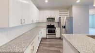 Located at 3841 Sandy Porter Rd in Charlotte, NC, this single-floor residence offers a thoughtfully designed layout with modern finishes throughout. The open-concept kitchen is a standout feature, showcasing crisp white cabinetry extending to the ceiling, granite countertops, a central island with an integrated sink, and a full suite of stainless steel appliances including a refrigerator with ice and water dispenser, electric range, over-the-range microwave, and dishwasher. A built-in wine rack adds a refined touch. Wood-style plank flooring flows throughout the main living areas, complementing the neutral, light-toned walls and creating a cohesive, contemporary aesthetic. The spacious living area is bright and open, with recessed lighting and pendant fixtures overhead. Bedrooms are carpeted for comfort, with multiple windows allowing generous natural light and views of the surrounding greenery. Ceiling fans provide additional comfort in the primary spaces. The bathroom features a double-sink vanity with matching granite countertops, white cabinetry, a large mirror, and a tub-shower combination. The overall design balances clean, modern styling with functional, livable spaces in a well-appointed Charlotte location.
