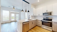 This well-designed two-bedroom, two-bathroom residence offers a thoughtfully utilized single-floor layout. The open-concept kitchen serves as a central highlight, featuring a peninsula island with a light stone countertop, an industrial-style matte black faucet, and a suite of stainless steel appliances including a refrigerator, electric range, microwave, and dishwasher. Upper white cabinetry pairs with warm wood-toned lower cabinets, complemented by a classic subway tile backsplash. Three stylish pendant lights hang overhead, extending visually into the adjacent living area, which is equipped with a ceiling fan and access to French doors that invite natural light.

The two bedrooms offer distinct finishes — one features light hardwood flooring, while the other is carpeted, both benefiting from tall ceilings and generous windows with outdoor views. Each room includes a dedicated closet. The two bathrooms are finished with large-format neutral tile; one includes a soaking tub with tiled surround, while the other features a walk-in glass-enclosed shower with a built-in niche. Clean white walls and consistent finishes throughout create a cohesive, modern aesthetic.