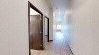 This one-bedroom, one-bathroom unit at 801 Second Ave N in Moorhead, Minnesota offers a well-designed, functional layout across a single floor. Light wood-style flooring runs throughout the entire unit, creating a cohesive and clean aesthetic. The open-concept living and kitchen area is bright and airy, featuring recessed lighting and tall ceilings that enhance the sense of space. The kitchen is equipped with stainless steel appliances, including a refrigerator, electric range, and over-the-range microwave, complemented by warm-toned wood cabinetry and a sink with ample counter space. A sliding glass door leads to a private balcony, allowing natural light to fill the main living area. The bedroom is a comfortable, quiet space with neutral walls, wood-style flooring, and a dedicated closet for storage. A hallway connects the main living spaces to the private areas of the unit. The bathroom features a walk-in shower with a white surround, chrome fixtures, and wood-style flooring, keeping the design consistent and clean. Throughout the unit, dark wood baseboards provide a grounding contrast to the light walls and floors, contributing to a polished, modern finish.