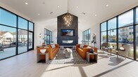 Located at 2700 E Overland Rd in Meridian, Idaho, this contemporary single-floor clubhouse offers a thoughtfully designed communal space defined by clean architectural lines, soaring vaulted ceilings, and an abundance of natural light. The entry hallway features dramatic floor-to-ceiling steel-framed glass walls and doors, setting a modern tone from the moment of arrival. Light hardwood flooring and large-format tile flow throughout, complementing the bright white walls and bold black-framed windows that frame outdoor views of the surrounding community.

The expansive living room serves as the centerpiece, anchored by a striking dark stone fireplace wall with a mounted display and a sculptural multi-bulb chandelier suspended from the peaked ceiling. Cognac leather sofas and curated décor create a welcoming yet sophisticated lounge atmosphere. Adjacent to the living room, the open dining area features a long communal wood table beneath cascading geometric pendant lights, paired with a large-island kitchen finished in navy cabinetry and white quartz countertops.

The space also includes dedicated conference rooms equipped with wall-mounted displays, wood tables, built-in shelving, and ample natural light — ideal for focused meetings or collaborative work. A game room with pool and ping pong tables, warm wood accent walls, and booth seating rounds out this well-appointed facility.