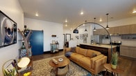 This single-story space showcases a thoughtfully designed open-concept layout where the living area flows seamlessly into the kitchen. The living room features rich hardwood-style flooring, recessed lighting, a striking arched floor lamp, and a bold blue sliding barn door that adds a distinctive design focal point. Large windows invite natural light throughout.

The kitchen is well-appointed with light wood cabinetry, quartz countertops, stainless steel appliances, a decorative tile backsplash, and a rustic wood-topped island with bar seating. Pendant lighting enhances the kitchen's warm, modern-industrial character.

Multiple bedrooms offer comfortable retreats, each featuring hardwood-style flooring, crisp white walls with bold black trim accents, and windows providing natural light. One bedroom includes direct exterior access through a glass-paneled door. Additional bedrooms offer closet access and restful, well-proportioned layouts.

The bathrooms are finished to a high standard, featuring dark wood vanities with illuminated mirrors, subway tile accents, teal tile details, sliding glass-enclosed tub-shower combinations with matte black hardware, and a separate water closet in the primary bath. The overall aesthetic balances contemporary design with warm, eclectic touches throughout.