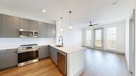 This thoughtfully designed single-floor unit offers a well-organized layout encompassing a kitchen, living room, bedroom, bathroom, office, and closet. Warm wood-look flooring flows consistently throughout, creating visual cohesion across the entire space.

The open-concept kitchen is a standout feature, equipped with full-height gray cabinetry, stainless steel appliances including a refrigerator, range, microwave, and dishwasher, and a white quartz peninsula with pendant lighting overhead. A white subway tile backsplash adds a clean, modern contrast to the gray cabinetry. The kitchen opens directly into the living area, which benefits from a ceiling fan and a glass door flanked by large windows that flood the space with natural light and offer exterior views.

The bedroom is a well-proportioned private retreat with dual windows providing additional natural light and outdoor views, complemented by a ceiling fan. It connects to a spacious walk-in closet outfitted with multi-tier wire shelving for generous storage.

The bathroom features an elongated dual-sink vanity with gray cabinetry, white quartz countertops, matte black fixtures, and large-format tile flooring. A dedicated office provides flexible space for work or additional use. A hallway with a double-door closet connects the living areas to the private rooms, completing a functional and modern floor plan.