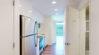Located on the 12th floor at 1335 Boylston Street in Boston's vibrant Fenway neighborhood, this one-bedroom, one-bathroom residence offers a thoughtfully designed layout with modern finishes throughout. Warm hardwood flooring runs continuously through the main living areas and bedroom, complementing the unit's clean, contemporary aesthetic.

The galley-style kitchen is outfitted with a full suite of stainless steel appliances, including a refrigerator, range with oven, built-in microwave, and dishwasher. White flat-panel cabinetry extends to the ceiling, maximizing storage, while white subway tile backsplash and light countertops contribute to a bright, polished look. Recessed lighting illuminates the space efficiently.

The generously sized bedroom is a standout feature, offering a spacious and airy atmosphere enhanced by a floor-to-ceiling sliding glass window wall that frames sweeping views of the surrounding cityscape. A built-in closet provides ample storage. The clean white walls and abundant natural light create a calm, inviting retreat.

The bathroom features large-format floor tiles in a neutral tone, a glass-enclosed walk-in shower with full subway tile surround, a wall-mounted vanity with mirror, and grab bar accessibility features. The overall design of the unit is modern and efficient, making excellent use of its compact footprint while maintaining a comfortable and functional living environment.