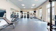 The fitness center at Shadow Creek in Jackson, Tennessee offers a comprehensive and thoughtfully equipped exercise facility designed to support a wide range of workout routines. The space is organized across a single floor and features a clean, modern aesthetic with neutral-toned walls, a drop-panel ceiling with recessed lighting, and durable rubber-speckled flooring throughout.

The cardio zone is well-stocked with multiple treadmills, elliptical trainers, and stair climbers, each equipped with individual monitors to keep users engaged during workouts. Large windows along the exterior walls allow generous amounts of natural light to fill the space, while also offering views of the surrounding Shadow Creek community. Full-length mirrors on one wall amplify the sense of openness and allow users to monitor their form.

A dedicated free weights area includes a multi-tiered dumbbell rack with a range of weights and an accompanying bench, ideal for strength training. A separate strength and functional training zone houses a multi-use cable and power rack system, along with a storage rack stocked with medicine balls, kettlebells, stability balls, and resistance bands, supporting functional and high-intensity training styles.

The facility also includes a water station for hydration convenience and direct outdoor access through a glass-panel door. Dual flat-screen TVs are mounted throughout the space for added entertainment. The overall ambiance is bright, clean, and practical.