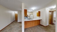 Located at 11581 Raven St NW in Coon Rapids, Minnesota, this two-bedroom, one-bathroom unit offers a practical and comfortable single-floor layout. The combined kitchen and living area forms the heart of the home, with the kitchen featuring a peninsula counter that separates the cooking space from the living area. The kitchen is equipped with wood-toned and white cabinetry, a white electric range, refrigerator, dishwasher, and a double sink — all set on tile flooring. The living room is carpeted and bright, with a sliding glass door that opens onto a private balcony overlooking the surrounding grounds and parking area. Baseboard heating runs throughout the carpeted living and bedroom areas, ensuring warmth during Minnesota winters, while a wall-mounted air conditioning unit provides cooling. The spacious primary bedroom features dual closets, a window with natural light, and plush carpeting. The second bedroom is similarly carpeted and well-lit. A hallway connects the main living areas to the full bathroom, which includes a tub/shower combo, toilet, and a vanity with a white countertop. A dedicated closet and entry hallway with tile flooring round out this efficiently designed unit.