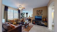 This 2-bedroom, 2-bathroom residence offers a comfortable and cohesive single-floor layout designed for both functionality and style. The open-concept living, dining, and kitchen area forms the heart of the home, featuring plush carpeting, ceiling fans, and large windows dressed with vertical blinds and layered drapes that fill the space with abundant natural light. The living room provides a generous gathering area, while the adjacent dining space accommodates a full dining set with room to spare.

The galley-style kitchen is well-equipped with stainless steel appliances, light wood cabinetry, granite-style countertops, and tile flooring. A dedicated laundry area with a full-size washer and dryer is conveniently accessible directly from the kitchen.

The primary bedroom is a comfortable retreat featuring a ceiling fan, a large window, and warm neutral tones accented by a taupe feature wall. The second bedroom mirrors this inviting aesthetic with similar finishes and ample natural light. Both bedrooms benefit from generous closet space, including a walk-in closet with built-in shelving and hanging rods.

The two bathrooms are finished with tile flooring, wood-toned vanity cabinetry, granite-style countertops, and well-lit mirrors. A hallway connects the private and shared areas of the home, completing a practical and polished floor plan.