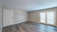 This single-floor residence offers a thoughtfully designed layout encompassing two bedrooms, two bathrooms, a kitchen, living room, closet, and hallway. The living room is a standout space, featuring dark hardwood-style flooring, neutral beige walls, and white baseboards that create a clean, modern aesthetic. French doors allow natural light to fill the room while providing outdoor access. The galley-style kitchen is well-equipped with white shaker cabinets featuring matte black hardware, white quartz countertops, a subway tile backsplash, stainless steel appliances, and light wood-style flooring. The bedrooms feature plush carpeting and neutral walls, with the primary bedroom offering a walk-in closet equipped with dual hanging rods. The bathrooms are finished with white cabinetry, quartz countertops, matte black fixtures, and striking marble-style tile accents. A louvered cabinet provides additional storage. The consistent use of neutral tones, modern hardware, and quality finishes throughout creates a cohesive and clean aesthetic across the entire unit.