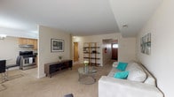 This single-floor unit is thoughtfully laid out to maximize functionality and comfort. The living room serves as the heart of the space, offering generous room for seating and relaxation. Plush wall-to-wall carpeting in a warm beige tone runs throughout, complemented by cream-colored walls that lend a bright, airy feel. A large sliding glass door floods the area with natural light and provides access to the outdoors. An open-frame shelving unit acts as a subtle room divider, adding visual depth without closing off the space.

The kitchen is efficiently designed with light maple cabinetry, granite-style countertops, and tile flooring. Stainless steel appliances — including a gas range, dishwasher, and refrigerator — provide a modern touch, while a pendant light fixture overhead adds warmth.

The bedroom is a serene retreat, featuring soft carpeting, a window with vertical blinds for adjustable natural light, and a double sliding-door closet offering ample storage. Additional doors connect to the bathroom and a secondary space, enhancing convenience.

The bathroom features a granite-topped vanity with a undermount sink, warm wood cabinetry, tiled walls with a decorative border accent, and a combined tub and shower area.