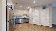 This studio presents a thoughtfully designed single-floor layout that maximizes every square foot with a clean, modern aesthetic. The kitchen is a standout feature, equipped with stainless steel appliances including a refrigerator, range, over-the-range microwave, and dishwasher. Two-tone cabinetry pairs light wood upper cabinets with slate gray lower cabinets, complemented by a subway tile backsplash and sleek dark countertops. Light wood-look flooring runs throughout the kitchen and transitions seamlessly into the open living area, which benefits from natural light streaming through French doors and flanking windows fitted with horizontal blinds. A ceiling fan overhead adds both function and style to the living space. The living area also features neutral warm-toned walls, offering a versatile backdrop for any décor. The bathroom is finished with large-format stone-look tile flooring, a tub-shower combo with white subway tile surround, and a wood-toned vanity with dark hardware. A dedicated closet with double doors provides practical storage. Recessed lighting throughout and crisp white trim and doors complete the polished, move-in-ready feel of this efficiently designed studio.