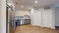 This studio presents a thoughtfully designed single-floor layout that maximizes every square foot with a clean, modern aesthetic. The kitchen is a standout feature, equipped with stainless steel appliances including a refrigerator, range, over-the-range microwave, and dishwasher. Two-tone cabinetry pairs light wood upper cabinets with slate gray lower cabinets, complemented by a subway tile backsplash and sleek dark countertops. Light wood-look flooring runs throughout the kitchen and transitions seamlessly into the open living area, which benefits from natural light streaming through French doors and flanking windows fitted with horizontal blinds. A ceiling fan overhead adds both function and style to the living space. The living area also features neutral warm-toned walls, offering a versatile backdrop for any décor. The bathroom is finished with large-format stone-look tile flooring, a tub-shower combo with white subway tile surround, and a wood-toned vanity with dark hardware. A dedicated closet with double doors provides practical storage. Recessed lighting throughout and crisp white trim and doors complete the polished, move-in-ready feel of this efficiently designed studio.