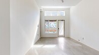 Located at 5460 N Interstate Ave in Portland's vibrant North Interstate corridor, this efficiently designed single-floor unit offers a clean, contemporary aesthetic throughout. The living room serves as the centerpiece of the space, characterized by soaring ceilings that amplify the sense of openness well beyond its compact footprint. Large sliding windows paired with a transom window above flood the room with natural light, while a glass-paneled entry door provides direct street access and an urban view that reflects the neighborhood's lively character. Polished concrete floors run continuously throughout the unit, lending an industrial-modern edge and a seamless visual flow between spaces. The kitchen is tucked neatly behind a partial wall partition, featuring white cabinetry, pendant lighting, and white appliances that maintain the unit's clean, minimalist palette. The bathroom is thoughtfully appointed with a single-basin vanity, standard fixtures, and concrete flooring consistent with the rest of the unit, along with a closet area that adds practical storage. Crisp white walls throughout create a bright, gallery-like ambiance, making the space feel fresh and versatile. This unit is well-suited for those seeking a modern, low-maintenance urban residence in North Portland.