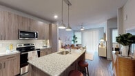 This single-floor residence at 1717 South Riverside Drive in Tulsa, Oklahoma, presents a thoughtfully designed open-concept layout with contemporary finishes throughout. The living area is bright and welcoming, featuring a ceiling fan, large sliding glass door with vertical blinds that invite natural light, and a neutral color palette that creates a calm, cohesive atmosphere.

The kitchen is a standout feature, outfitted with warm wood-tone cabinetry extending to the ceiling, granite countertops, stainless steel appliances including a refrigerator, electric range, and microwave, and a spacious island with a single-basin sink and pendant lighting overhead. Dark hardwood-style flooring runs through the kitchen and main living areas, adding visual warmth and continuity.

The bedroom is carpeted and comfortably sized, offering ample natural light through a large window with blinds and drapery, along with ceiling fan fixtures. The en-suite bathroom features a glass-enclosed shower with tile surround, a wood-grain vanity with granite countertop, dual sinks, and a backlit mirror. A washer and dryer are also included within the unit, adding everyday convenience to this well-finished Tulsa residence.
