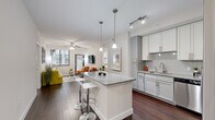 Located at 7850 Pasadena Blvd in Pembroke Pines, FL, this well-appointed single-floor residence offers a contemporary open-concept layout designed for comfortable living. The kitchen is a standout feature, showcasing white shaker cabinetry, gray lower cabinets, a subway tile backsplash, granite countertops, and a full suite of stainless steel appliances including a refrigerator, range, microwave, and dishwasher. A central island with granite countertop and bar seating serves as both a functional workspace and a casual dining spot, illuminated by pendant lighting overhead. Track lighting adds additional brightness throughout the kitchen. Rich, dark hardwood-style flooring flows seamlessly from the kitchen into the open living area, which features a ceiling fan, large windows with blinds, and a glass door that allows an abundance of natural light. The bedroom is carpeted for comfort and includes a ceiling fan and windows that bring in soft, natural light. A walk-in closet with built-in shelving provides generous storage. The bathrooms are finished with marble-style tile flooring; one includes a soaking tub with shower and a vanity, while another features a glass-enclosed walk-in shower. The overall palette of soft whites and grays lends the space a clean, modern ambiance throughout.