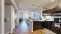 This single-floor residence offers a thoughtfully designed open-concept layout that seamlessly connects the kitchen, dining, and living areas. The kitchen is a standout feature, equipped with rich dark cabinetry, light granite-style countertops, black appliances including a refrigerator, range, microwave, and dishwasher, and under-cabinet lighting. A peninsula with bar seating and pendant lighting above serves as both a functional workspace and a casual dining spot, making it ideal for entertaining.

The living area flows naturally from the kitchen and is bathed in natural light through a full-length sliding glass door that opens to a private balcony. A ceiling fan overhead adds comfort to the space. Warm hardwood-style flooring runs throughout the main living areas, adding a cohesive and inviting aesthetic.

The bedroom is a calm retreat featuring plush carpeting, a ceiling fan, and a large window that brings in abundant natural light. It connects directly to a well-sized bathroom appointed with dark cabinetry, a wide vanity with light stone countertops, a large framed mirror, and hardwood-style flooring. The overall ambiance of the residence is modern and comfortable, with a neutral color palette that lends itself to a variety of interior styles.