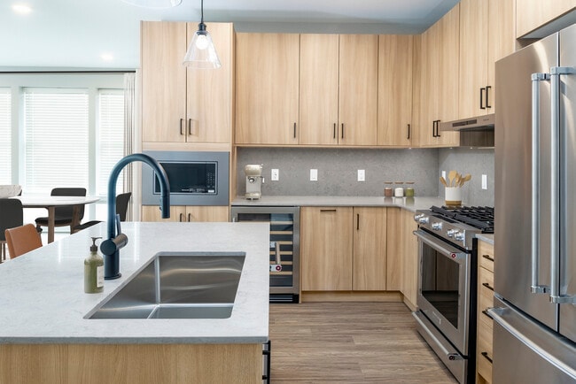 Signature Collection kitchen with stainless steel appliances (wine fridge included), quartz countertops, quartz tile backsplash, oak cabinetry, and hard-surface flooring - Avalon Parsippany