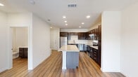 Located at 201 Wildwood Blvd in Forney, TX, this single-story, one-bedroom, one-bathroom residence offers a thoughtfully designed layout that maximizes functionality and style. The open-concept kitchen serves as the centerpiece of the home, showcasing rich dark-brown cabinetry with sleek hardware, light granite countertops, a central island ideal for dining or prep work, and a full suite of stainless steel appliances including a refrigerator, dishwasher, and electric range. Recessed lighting and wood-look flooring add a modern, polished finish to this space. The kitchen flows naturally into the living area, which benefits from a ceiling fan and a window that allows natural light to brighten the room. The spacious primary bedroom features plush carpet, a ceiling fan with a light fixture, and a window with neighborhood views. A generously sized walk-in closet offers built-in shelving and hanging rods, providing ample storage. The bathroom is well-finished with a dark-vanity cabinet, white quartz countertop, and a full tub-shower combo featuring large-format neutral tile surround. A dedicated hallway connects all rooms efficiently, completing this practical and attractive single-floor home.