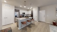This well-designed single-floor residence offers a thoughtful layout that seamlessly connects its key living spaces. The kitchen is a standout feature, showcasing a striking two-tone cabinetry scheme — crisp white upper cabinets paired with dark wood-finish lower cabinets — complemented by granite countertops, a stone tile backsplash, and a full suite of stainless steel appliances including a refrigerator, electric range, and microwave. A center island with additional granite countertop space and seating for multiple bar-height chairs makes it ideal for casual dining and entertaining.

The living area is bathed in natural light through large sliding glass doors dressed with layered curtains, and features light wood-look flooring that runs throughout the residence. A ceiling fan adds both style and function to the space.

The bedroom is a serene retreat, with generous windows fitted with blinds and patterned drapes that allow for adjustable natural light. A ceiling fan overhead and light wood flooring contribute to the room's airy, comfortable ambiance.

The bathroom is clean and functional, featuring a granite-topped vanity with white cabinetry, light tile flooring, and a shower-tub combination. A hallway connects the bathroom to additional closet or storage space, enhancing the overall practicality of the residence.