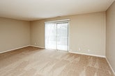 This single-floor residence offers a practical and comfortable layout designed for everyday living. The spacious living area is finished with soft, neutral-toned carpet and features a large sliding glass door dressed with vertical blinds, allowing natural light to fill the room while providing access to the outdoors. The flooring transitions to rich, dark hardwood-style planks in the kitchen, which is well-appointed with white cabinetry, granite-style countertops, a full suite of white appliances including an electric range, dishwasher, and refrigerator, plus an under-cabinet range hood and a double-basin sink. A peninsula counter adds additional workspace and visual separation from the adjoining area. The bedrooms are generously sized, each featuring plush carpet, vertical-blind windows that invite natural light, and ceiling fans for comfort. The bathroom is finished with stone-look tile flooring, white cabinetry with a light stone countertop, a single vanity sink, and a full tub-shower combination with white tile surround. Warm, neutral wall tones carried throughout the space create a cohesive and inviting atmosphere from room to room.