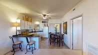 This thoughtfully designed one-bedroom, one-bathroom residence is laid out entirely on a single floor, offering an efficient and comfortable living arrangement. The open-concept kitchen and living area serves as the heart of the home, featuring a kitchen equipped with white cabinetry, dark granite countertops, a breakfast bar with bar seating, and standard appliances including a range, microwave, and refrigerator. Tile flooring runs throughout the kitchen and dining area, where there is ample space for a full dining set. Ceiling fans are present in both the kitchen and living areas, contributing to comfortable airflow throughout. The living room is carpeted and benefits from a large window that allows natural light to filter in, creating a bright and welcoming atmosphere. The spacious primary bedroom is carpeted and features a ceiling fan, a sizable window with outdoor views, and direct access to both a walk-in closet with wire shelving for generous storage and a full bathroom. The bathroom includes a combination tub and shower enclosed with sliding glass doors and tile flooring. The walk-in closet provides substantial storage capacity with multi-level wire shelving systems. Overall, the residence offers a practical and comfortable layout suited for everyday living.
