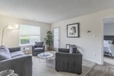 Located at 5800 Trellis Arch in Virginia Beach, VA, this single-floor residence offers a well-organized layout with distinct living, sleeping, and functional spaces. The living room is bright and welcoming, featuring large windows and a glass door that invite natural light and provide outdoor views of surrounding greenery. Neutral-toned carpet and light walls create a clean, open atmosphere throughout the space.

The galley-style kitchen is efficiently designed with dark cabinetry, wood-look flooring, and black appliances including a refrigerator and electric range. A breakfast bar area connects the kitchen to the main living space, allowing for easy interaction between rooms. Adjacent storage and closet space adds to the unit's functionality.

The bedrooms are carpeted and generously proportioned, each offering natural light through windows with blinds. One bedroom includes a walk-in closet with built-in shelving, while another features a dresser alcove and mirror. Both provide a quiet, restful setting.

The bathroom includes dark cabinetry with a single-sink vanity, wood-look flooring, and a shower/tub combination. The overall design throughout the home is practical and neutral, offering a comfortable living environment in a well-situated Virginia Beach location.