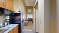 Located at 225 112th Ave NE in the heart of Bellevue, WA, Loft 335 is a thoughtfully designed one-bedroom, one-bathroom residence that maximizes its compact footprint through a striking two-story loft layout. The main level welcomes you with a functional kitchenette equipped with stainless steel appliances, warm wood cabinetry, and ample counter space. From here, a corridor opens into the living area, which features patterned carpeting and a dedicated workspace with a built-in desk positioned beneath stacked windows that draw in natural light. The soaring ceiling height is a standout architectural feature, creating an open, airy ambiance that makes the space feel considerably larger than its footprint suggests. A ceiling fan with integrated lighting anchors the upper loft level, which houses the private bedroom. The bedroom is a serene retreat, appointed with neutral tones, a full-sized bed with crisp white linens, and a framed wall accent. The full bathroom is clean and efficiently arranged, featuring a combined tub and shower, a wall-mounted sink, a medicine cabinet mirror, and tile flooring. A closet completes the unit's layout. The dual-level design of this Bellevue loft offers a smart, functional living solution in a well-connected urban location.