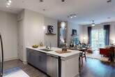 This well-appointed single-floor residence showcases a contemporary design with a thoughtful, open-concept layout. The kitchen is a standout feature, offering a galley-style cooking area equipped with stainless steel appliances, a smooth-top range, microwave, and white subway tile backsplash. Two-toned cabinetry — white uppers paired with slate-gray lowers — frames crisp white quartz countertops. A large central island extends into the living space, accented by stylish pendant lighting, and includes a double undermount sink and integrated dishwasher, making it ideal for both meal prep and casual dining.

The open living and dining area features warm hardwood-style flooring, a ceiling fan, and a decorative floating shelf above a media console. A sliding glass door floods the space with natural light and opens directly onto a private balcony with outdoor views.

The primary bedroom offers plush carpeting, a large window with outdoor views, and a ceiling fan, while the secondary bedroom mirrors the same comfortable aesthetic. The primary bathroom features marble-look tile flooring, a frameless glass shower, a wide vanity with white quartz countertop, and direct access to a walk-in closet. A second full bathroom includes a tiled tub-shower combination and a sleek single-basin vanity.