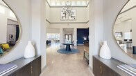 This generously sized single-floor amenity center offers a well-rounded selection of community spaces designed for both relaxation and recreation. The grand entrance lobby immediately impresses with soaring double-height ceilings, clerestory windows that flood the space with natural light, polished concrete floors, and a striking orb chandelier suspended above a central round table. Accent walls in deep navy blue lend a sophisticated contrast to the crisp white walls throughout.

The lounge area features expansive floor-to-ceiling sliding glass doors that open to an outdoor terrace, offering seamless indoor-outdoor living with views of the surrounding grounds. Plush seating arrangements and a wall-mounted TV make this an inviting gathering space.

The fitness center is a standout feature, divided into dedicated cardio and strength training zones. The cardio area is lined with treadmills, ellipticals, and stationary bikes alongside full-length mirrors and teal accent walls, while the strength zone is equipped with Precor cable machines, free weights, and functional training equipment—all bathed in natural light from large windows.

A game and social lounge rounds out the amenities, complete with a pool table, high-top seating, a mounted TV, and a fully equipped kitchenette featuring stainless steel appliances, mosaic tile backsplash, and ample cabinetry—ideal for community gatherings.
