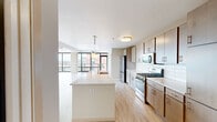 This well-appointed 2-bedroom, 2-bathroom unit offers a thoughtfully designed single-floor layout with a bright, open-concept living space. The expansive living room is defined by dramatic floor-to-ceiling windows on two walls, framing panoramic views of the surrounding cityscape and greenery beyond, while light hardwood-style flooring flows seamlessly throughout the entire unit. A striking exposed concrete column adds an industrial architectural touch to the airy living area.

The kitchen is both functional and stylish, featuring light wood cabinetry extending to the ceiling for ample storage, a white subway tile backsplash, quartz countertops, a large center island with a built-in sink and pendant lighting, and a full suite of stainless steel appliances including a gas range, microwave, and refrigerator.

The primary bedroom offers a comfortable, well-proportioned retreat with a ceiling fan and access to a closet. The second bedroom is similarly bright and open, with its own closet access. Both bathrooms are finished in a clean, contemporary style, with one featuring a walk-in tiled shower with a built-in niche and open wood shelving for added storage convenience. Two dedicated closets provide practical everyday storage throughout the unit.