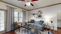 Located along Highway 105 in Montgomery, TX, this single-floor, one-bedroom, one-bathroom residence offers a thoughtfully designed layout that maximizes both function and comfort. The open-concept kitchen and living area serves as the heart of the home, anchored by rich hardwood-style flooring that flows throughout the main spaces. The kitchen is equipped with dark espresso cabinetry, granite-style countertops, stainless steel appliances including a full-size refrigerator, a deep double-basin sink, subway tile backsplash, and a peninsula with pendant lighting and bar seating — ideal for casual dining or entertaining. The living room features elegant crown molding, a ceiling fan, and multiple windows that invite natural light, creating a bright and welcoming atmosphere. The bedroom is a comfortable retreat with plush carpeting, dual windows with views of the surrounding greenery, a ceiling fan, and direct access to a closet. The full bathroom offers a tub-shower combination with tiled surround, dark wood vanity with a white countertop, and hardwood-style flooring. A dedicated laundry area with wire shelving adds everyday convenience. The entrance and hallway provide a smooth transition between all areas of this well-organized, efficiently planned residence.