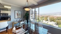 Located in the heart of Los Angeles, this well-appointed residence at 6200 W 3rd St offers a refined living experience with sweeping city views visible from nearly every room. The interior is defined by a cohesive blue and gray color palette complemented by crisp white crown molding and warm parquet hardwood flooring throughout the main living areas.

The living room makes a bold statement with a deep navy accent wall, elegant crown molding, and curated Los Angeles-themed artwork. It flows naturally into the dining area, where a large floor-to-ceiling window frames stunning elevated views of the cityscape, and a statement pendant light anchors a glass dining table.

The kitchen features white cabinetry with sleek hardware, stainless steel countertops, and a window that continues the home's connection to the outdoors. A breakfast bar with granite countertop and in-unit laundry add practicality to the space.

The primary bedroom is generously sized with multiple windows offering broad city views, soft carpet, and a serene blue color scheme. A second bedroom provides a cozy retreat with its own window view and warm accent wall. Both bathrooms are finished with classic white tile surrounds and tub-shower combinations, maintaining a clean and timeless aesthetic throughout this elevated Los Angeles home.