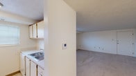 This single-floor unit on Hermitage Hills Blvd in Hermitage, Pennsylvania, offers a straightforward, functional layout across several distinct areas. The floor plan, as visible in the overhead scan, organizes the living space, kitchen, bedroom areas, and bathroom in a logical, connected arrangement.

The kitchen is positioned near the entrance and is equipped with wood-trimmed upper cabinetry, a double-basin sink, a coil-burner electric range, and a full-size refrigerator. A wall-mounted thermostat is conveniently located nearby at the kitchen-to-living area transition.

The living area is generously proportioned, featuring neutral-toned carpet, white walls, and a textured ceiling. Multiple electrical outlets are present along the walls, and the space flows openly from the kitchen partition.

The bedroom areas are carpeted and finished with the same light, neutral palette. Windows fitted with horizontal blinds allow natural light to filter in, contributing to a bright atmosphere. Visible ceiling vents indicate a central air system serving the space.

The bathroom is cleanly appointed with tile flooring, a single-sink vanity with a laminate countertop, a mirror-front medicine cabinet, a toilet, and a tub-shower combination with a curtain rod.

Overall, the unit presents a clean, utilitarian design well-suited for comfortable everyday living.