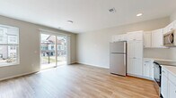 This thoughtfully designed two-floor residence offers 1 bedroom and 1 bathroom across a well-utilized layout. The main level hosts the combined kitchen and living area, which is bright and open, finished with light hardwood-style flooring throughout. The kitchen is equipped with stainless steel appliances — including a refrigerator, range, over-the-range microwave, and dishwasher — complemented by white shaker-style cabinetry, clean white countertops, and a tile backsplash. The adjacent living area receives generous natural light through a large sliding glass door that opens to a private balcony with views of the surrounding neighborhood. A secondary window adds additional brightness to the space. Carpeted stairs lead to the lower level, where the bedroom, bathroom, and closet are located. The bedroom features plush carpeting, a ceiling fan, and a horizontal window that brings in natural light. A sliding closet door provides access to dedicated storage with built-in shelving. The full bathroom includes a clean, white tub-shower combination. The space maintains a neutral, modern palette throughout, creating a cohesive and functional living environment suited for everyday comfort.