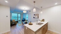 This well-appointed two-bedroom, two-bathroom residence in Calgary, AB offers a thoughtfully designed open-concept layout finished with light hardwood flooring throughout. The kitchen serves as a central hub of the home, anchored by a generous island with a white quartz countertop, an undermount double sink, and pendant lighting overhead. Light wood cabinetry extends to the ceiling, complemented by stainless steel appliances including a range, microwave, and refrigerator. The kitchen flows seamlessly into the dining and living areas, where floor-to-ceiling windows and a glass balcony door frame sweeping views of the Calgary cityscape. The living room offers direct balcony access, bathing the space in natural light. The primary bedroom is a serene retreat featuring a large corner window with panoramic views, a sliding-door closet, and light neutral finishes. The second bedroom mirrors the calm aesthetic with similar quality finishes. Both bathrooms are modern and clean, with the main bath showcasing a glass-enclosed walk-in shower, a wood-toned vanity with white countertop, and hexagonal tile accents. A hallway connects all rooms efficiently, contributing to the unit's practical and polished overall design.