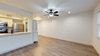 This single-story space offers a clean, modern interior defined by consistent wood-look flooring and a neutral white color palette throughout. The open-concept living and dining area is anchored by a ceiling fan with integrated lighting and recessed fixtures, creating a bright and airy atmosphere. A pass-through kitchen counter connects the living area to the kitchen, which is equipped with stainless steel appliances including a gas range, microwave, and refrigerator, complemented by white cabinetry, a decorative tile backsplash, and a light quartz countertop with an undermount sink. Built-in shelving adjacent to the kitchen provides additional storage and display space. The entryway features a modern door with frosted glass panels and a window that allows natural light to filter in. Additional rooms include generously sized bedrooms, each with ceiling fans and windows overlooking greenery. The bathroom is thoughtfully finished with herringbone-patterned tile in the shower surround, wood-look tile flooring, and a contemporary vanity, creating a cohesive and refined aesthetic throughout the space.