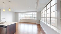 Located at 10 Lafayette Square in the heart of downtown Buffalo, this well-appointed one-bedroom, one-bathroom residence offers a thoughtfully designed open-concept layout across a single floor. The combined kitchen and living area forms the heart of the unit, bathed in abundant natural light streaming through expansive multi-pane grid windows that frame sweeping views of the Buffalo cityscape, including notable downtown architecture. Rich hardwood flooring runs throughout, adding warmth and continuity to the space. The kitchen is outfitted with sleek dark-wood cabinetry, light quartz countertops, a center island with an undermount sink, and a full suite of stainless steel appliances including a refrigerator, range, over-the-range microwave, and dishwasher. Pendant lighting above the island adds a refined touch. The generous living area offers an airy, open feel accentuated by recessed lighting and clean white walls. The bedroom features hardwood floors, a ceiling fan, and direct access to a closet. The bathroom includes a dark-wood vanity with a stone-topped countertop, a large mirror with modern lighting, and neutral tile flooring. A sleek, modern aesthetic defines the entire residence.