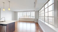 Located at 10 Lafayette Square in the heart of downtown Buffalo, this well-appointed one-bedroom, one-bathroom residence offers a thoughtfully designed open-concept layout across a single floor. The combined kitchen and living area forms the heart of the unit, bathed in abundant natural light streaming through expansive multi-pane grid windows that frame sweeping views of the Buffalo cityscape, including notable downtown architecture. Rich hardwood flooring runs throughout, adding warmth and continuity to the space. The kitchen is outfitted with sleek dark-wood cabinetry, light quartz countertops, a center island with an undermount sink, and a full suite of stainless steel appliances including a refrigerator, range, over-the-range microwave, and dishwasher. Pendant lighting above the island adds a refined touch. The generous living area offers an airy, open feel accentuated by recessed lighting and clean white walls. The bedroom features hardwood floors, a ceiling fan, and direct access to a closet. The bathroom includes a dark-wood vanity with a stone-topped countertop, a large mirror with modern lighting, and neutral tile flooring. A sleek, modern aesthetic defines the entire residence.