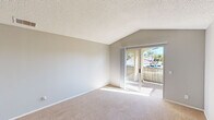 This efficient and thoughtfully designed single-floor residence offers a comfortable layout comprising a kitchen, living room, bedroom, bathroom, and two hallways. The open kitchen is equipped with stainless steel appliances—including a range, over-the-range microwave, and French door refrigerator—complemented by crisp white cabinetry, recessed lighting, and light wood-tone flooring that extends into the adjoining living area. A breakfast bar with a neutral stone-finish countertop provides a seamless transition between the kitchen and living space, where a ceiling fan adds comfort and a vaulted ceiling creates an airy, open feel. Sliding glass doors flood the living room with natural light and open directly onto a private balcony with outdoor views. The bedroom is carpeted and features a large window with vertical blinds, allowing ample natural light, along with a spacious sliding-door closet offering generous storage. Neutral gray walls and textured ceilings are consistent throughout, lending the space a clean and cohesive aesthetic. The bathroom includes a wide vanity with white cabinetry, a large mirror, a well-lit three-bulb fixture, and a shower-tub combination, providing practical functionality in a tidy, neutral-toned setting.