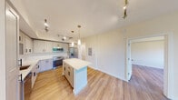 This well-designed single-floor residence offers a clean, contemporary aesthetic throughout, combining modern finishes with a bright and open layout. The kitchen serves as the centerpiece of the space, showcasing light shaker-style cabinetry with matte black hardware, crisp white quartz countertops, and a classic white subway tile backsplash. A generous center island provides additional prep space and casual seating, while pendant lighting with brass accents adds a refined touch overhead. Stainless steel appliances, including a French door refrigerator, electric range, built-in microwave, and dishwasher, complete the fully equipped kitchen. Track lighting runs throughout the main living area, which flows seamlessly from the kitchen and benefits from abundant natural light. Light-toned hardwood-style flooring extends across the living spaces, lending warmth and continuity. The bedrooms are tranquil and spacious, with one featuring a large window overlooking serene water and greenery, and another offering sliding glass door access to a private balcony with lush outdoor views. The bathroom is finished with neutral tile flooring, a wide vanity with under-cabinet storage, and a large mirror. The overall ambiance is clean, modern, and move-in ready.