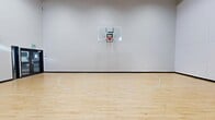 Located in Calgary, AB, this indoor basketball court offers a spacious, well-designed facility built for both recreational and competitive use. The court spans a generously sized single-floor area, providing ample room for full gameplay and training activities. The standout feature is the classic light maple hardwood floor, finished with crisp white court markings including three-point arcs, key zones, and boundary lines — all maintained in excellent condition. Two wall-mounted basketball hoops with transparent acrylic backboards and red rims are positioned at each end of the court, meeting standard play requirements. The perimeter walls are lined with large, segmented white padding panels, offering both safety and a clean, modern aesthetic. The ceiling soars to an impressive height, creating a bright and open atmosphere that accommodates high-arc shots and unrestricted movement. Natural light filters into the space through a series of rectangular clerestory windows positioned near the top of the walls, supplementing the overhead lighting and giving the court an airy feel. A set of double glass doors with clearly marked exit signage provides convenient access to the court. The overall design is clean, functional, and purpose-built, making this an excellent facility for basketball enthusiasts of all skill levels.