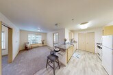 Located at 13000 Linden Ave N in Seattle's Shoreline neighborhood, this two-bedroom, one-bathroom residence offers a practical and well-organized single-floor layout. The open-concept kitchen is a central feature, equipped with light wood cabinetry, granite-style laminate countertops, a built-in dishwasher, electric range, and a peninsula breakfast bar with seating — ideal for casual dining. The kitchen flows seamlessly into the carpeted living room, which receives natural light through large windows overlooking the surrounding building complex. Light wood vinyl flooring runs throughout the kitchen and bathroom areas, creating a clean contrast with the soft carpet in the living and sleeping spaces. Both bedrooms are bright and comfortably proportioned, each featuring large windows with exterior views and baseboard heating. Sliding light wood closet doors provide generous storage in the bedrooms. The full bathroom is neatly finished with wood-tone cabinetry, a granite-style vanity top, a tub-shower combination, and easy-care vinyl flooring. With four closets distributed throughout the unit, storage is notably practical. The neutral color palette and consistent finishes give the space a cohesive, functional character suited for everyday living in Seattle.