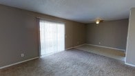 This single-floor space offers a practical and comfortable layout designed for everyday living. The main living area is finished with wall-to-wall carpeting in a neutral tone, providing a soft and inviting feel underfoot. Warm beige walls create a cohesive, understated ambiance throughout the space.

A standout feature of the living area is the large sliding glass door dressed with vertical blinds, which allows an abundance of natural light to fill the room while offering direct access to the outdoors. The bright, diffused light coming through the blinds enhances the open and airy character of the space.

A ceiling fan is installed overhead, contributing to both comfort and air circulation throughout the year. The textured ceiling adds a classic, finished touch to the interior. Clean white baseboards frame the carpeted floor neatly, adding a crisp contrast to the neutral wall color.

Overall, this space presents a straightforward and functional environment with key features that support comfortable, day-to-day use. The combination of natural light, neutral finishes, and practical amenities makes it a well-rounded and move-in ready space suitable for a variety of needs.