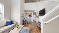 This two-story home makes a striking first impression with its dramatic double-height ceilings in the main living area, creating an airy, open atmosphere that feels remarkably spacious. The ground floor hosts the primary living spaces, where warm hardwood-style flooring flows seamlessly through the living room, dining area, and kitchen. Large windows invite an abundance of natural light, enhancing the bright, neutral color palette throughout. The kitchen features white cabinetry, a clean countertop with an undermount sink, subway tile backsplash, and stainless steel appliances, with a pantry nearby for additional storage. A dedicated laundry room with built-in shelving adds everyday convenience. A staircase leads to the upper level, which is home to two bedrooms, two full bathrooms, two closets, and a hallway. The primary bedroom offers a private retreat with a walk-in closet fitted with wire shelving. The secondary bedroom is cozy and well-lit, featuring a large window with natural views. Both bathrooms are finished with white vanities, wide mirrors, and wood-style flooring. The overall design is clean, modern, and functional, offering a comfortable and well-organized layout suited for everyday living.