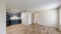 This single-floor residence offers a practical and comfortable layout designed for everyday living. The open living area greets you at the entrance, featuring durable wood-look plank flooring, neutral-toned walls, and a textured ceiling that adds subtle character. Natural light filters in through windows fitted with blinds, creating a bright and welcoming atmosphere throughout.

The kitchen is efficiently designed with dark navy cabinetry, a stainless steel sink, light-toned countertops, and a black electric range with an overhead ventilation hood. The wood-look flooring continues seamlessly from the living area into the kitchen, maintaining a cohesive aesthetic.

The bedrooms are carpeted for comfort and warmth. The primary bedroom is a standout, featuring a ceiling fan, access to a walk-in closet, and a dedicated vanity area complete with dark cabinetry, a round undermount sink, granite-style countertops, and a large wall mirror. The bathroom includes a full tub-and-shower combination finished with clean white tile surround.

Throughout the space, consistent design choices — including the navy cabinetry, neutral walls, and warm flooring tones — create a cohesive and functional living environment well-suited for comfortable, day-to-day use.