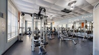 Located at 8151 Patterson Woods Dr in Orlando, FL, this fitness center offers a thoughtfully organized exercise space across a single floor. The room is finished with a drop-panel ceiling, resilient rubber flooring, and soft blue-gray walls adorned with large motivational typography — including words like "Run," "Lift," "Power," "Commitment," "Focus," "Energy," "Goals," and "Fitness" — creating an energizing atmosphere throughout.

Natural light streams in through multiple large windows fitted with horizontal blinds, providing views of the surrounding greenery and keeping the space feeling open and airy. Full-length mirrors along the walls further enhance the sense of depth and allow users to monitor their form during workouts.

The cardio section is well-stocked with Life Fitness treadmills, elliptical trainers, upright and recumbent stationary bikes, and stair climbers. The strength training area features a multi-station cable machine, a variety of weight benches, squat racks, and a full dumbbell rack with a wide range of free weights. A wall-mounted flat-screen television adds convenience for entertainment during workouts. The space is designed to accommodate a broad range of fitness routines, from high-intensity cardio sessions to comprehensive strength training programs.