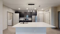 Located at 14680 Westerly Dr in Winter Garden, Florida, this single-floor residence offers a well-designed layout with modern finishes throughout. The kitchen serves as the centerpiece of the home, featuring bold dark cabinetry, a classic white tile backsplash, and a full suite of stainless steel appliances including a refrigerator, range, and built-in microwave. A large white quartz-topped island with an integrated sink and matte black faucet provides generous prep space and anchors the open-concept kitchen area. Globe pendant lights hang above the island, adding a stylish touch. The living area is bright and welcoming, with wood-look flooring, a ceiling fan, and windows that invite natural light while offering views of the surrounding neighborhood. The bedrooms are carpeted for comfort, each featuring windows with blinds and closet space. The bathrooms are finished in a clean, contemporary style with dark vanity cabinetry, white countertops, large-format marble-look tile surrounding the tub-shower combinations, and coordinating matte black fixtures. Light wood-tone flooring in the bathrooms completes the cohesive aesthetic. An in-unit laundry area is also present, adding everyday convenience to this thoughtfully appointed home.
