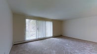 Located at 2661 Willits Road in the Somerton neighborhood of Philadelphia, PA, this single-floor unit offers a clean and functional layout designed for comfortable everyday living. The living area is a standout feature, highlighted by expansive sliding glass doors framed with vertical blinds that allow abundant natural light to fill the room. The large glazed opening provides views of the surrounding neighborhood and creates a seamless connection between the interior and the outdoors. A baseboard heating system runs along the base of the exterior wall, ensuring efficient climate control throughout the colder months. The floors are covered in neutral-toned carpeting that lends a soft, understated feel to the space. The walls are finished in a light, warm beige tone, contributing to the bright and airy atmosphere of the interior. The smooth white ceiling completes the clean aesthetic, keeping the space feeling open and uncluttered. The overall design is straightforward and practical, providing a versatile canvas that can accommodate a variety of furniture arrangements and personal styles. This single-story layout offers ease of accessibility and a cohesive flow throughout the unit.