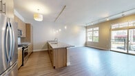 Located at 11127 N Weston Dr in Mequon, Wisconsin, this well-appointed three-bedroom, two-bathroom residence offers a thoughtfully designed single-floor layout that balances comfort and functionality. The open-concept kitchen and living area serves as the heart of the home, featuring warm wood-tone cabinetry, stainless steel appliances, a mosaic tile backsplash, and a large granite-topped island with pendant lighting — ideal for both everyday living and entertaining. Hardwood-style flooring flows throughout the main living areas, complemented by track lighting that enhances the clean, modern aesthetic. Sliding glass doors open to a private balcony, inviting in natural light and outdoor views of the surrounding streetscape. The spacious primary bedroom includes a dedicated walk-in closet with wire shelving and a well-appointed en suite bathroom featuring a soaking tub with glass-enclosed shower combo and large-format tile flooring. Additional bedrooms are carpeted, bright, and served by ceiling fans, with generous closet space. A second bathroom offers a sleek glass-enclosed walk-in shower with tile surround. Four total closets and a utility room provide ample storage throughout this polished, move-in-ready residence.