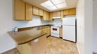 This single-floor unit is laid out to maximize functionality across its living spaces. The living area is generously sized, featuring wall-to-wall tan carpeting, crisp white walls, and a sliding glass door fitted with vertical blinds that floods the room with natural light while providing direct outdoor access. A flush-mount ceiling light provides additional illumination, and clean white baseboards frame the space throughout.

The kitchen is well-equipped, featuring light wood cabinetry with ample upper and lower storage, dark laminate countertops, and a peninsula that offers added prep space and a casual dining option. White appliances—including a refrigerator, electric range, and under-cabinet range hood—are paired with a double-basin sink. Tile flooring and a large overhead skylight panel keep the kitchen bright and easy to maintain.

The bedrooms are carpeted and finished with white walls, each featuring windows with outdoor views and flush-mount ceiling lighting. The two bathrooms include tile flooring and tub-shower combinations. One bathroom features a single-sink vanity with wood cabinetry, a large mirror, and a bathtub. The second is similarly appointed with a full tub-shower surround and clean, simple finishes throughout.